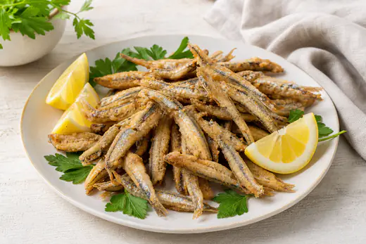 Alici impanate dorate e croccanti disposte su un piatto, con spicchi di limone e ciuffi di prezzemolo