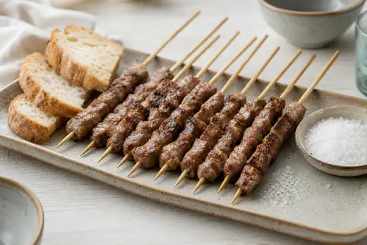 Arrosticini abruzzesi dorati su stecchi di legno, con piccoli cubetti di carne sgrassata, serviti su un vassoio con pane e sale grosso