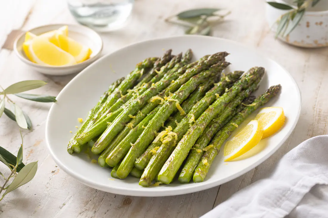 Asparagi verdi arrostiti con le punte leggermente dorate, disposti su un piatto bianco con scorza di limone