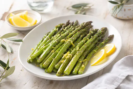 Asparagi verdi arrostiti con le punte leggermente dorate, disposti su un piatto bianco con scorza di limone