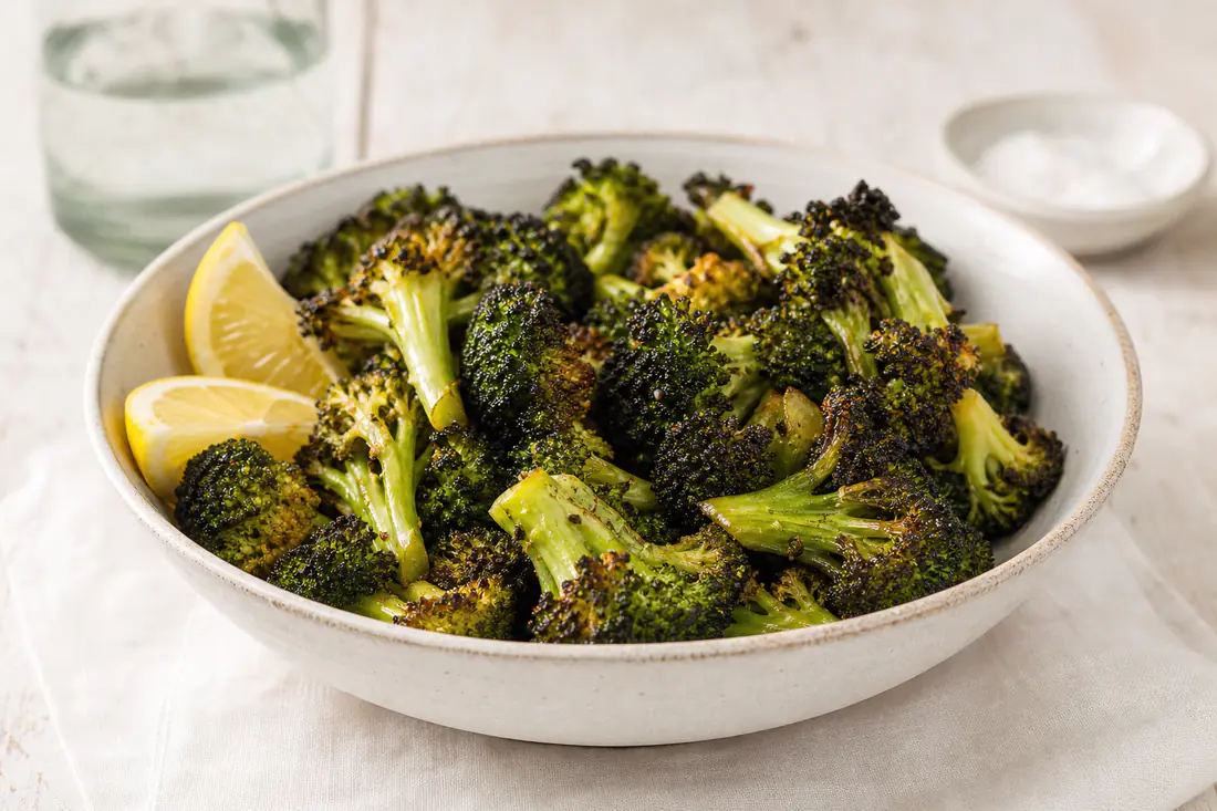 Cimette di broccoli arrostite con le punte scure e croccanti e il gambo verde, servite in una ciotola con limone