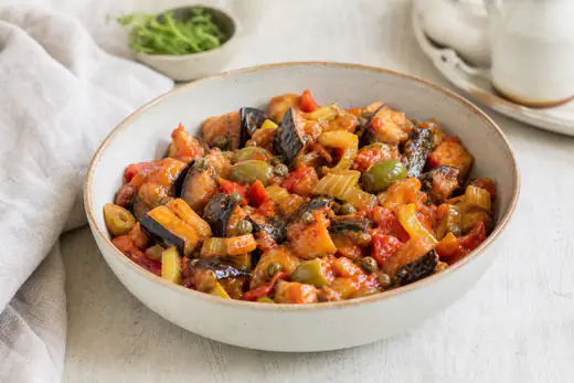 Caponata siciliana con cubetti di melanzane dorate, sedano, olive verdi e capperi in salsa agrodolce di pomodoro, in una ciotola di ceramica