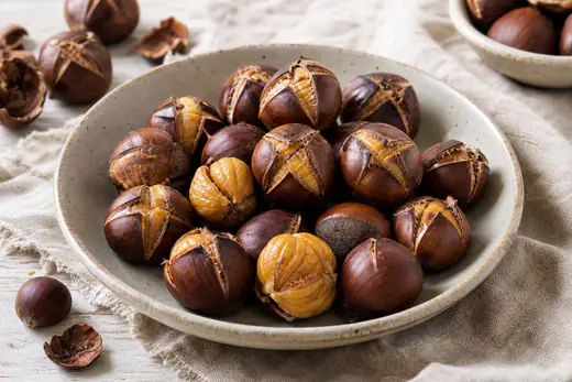 Castagne arrostite con il taglio a croce e la buccia lucida aperta a fiore, qualcuna sbucciata con la polpa gialla, su un canovaccio di lino