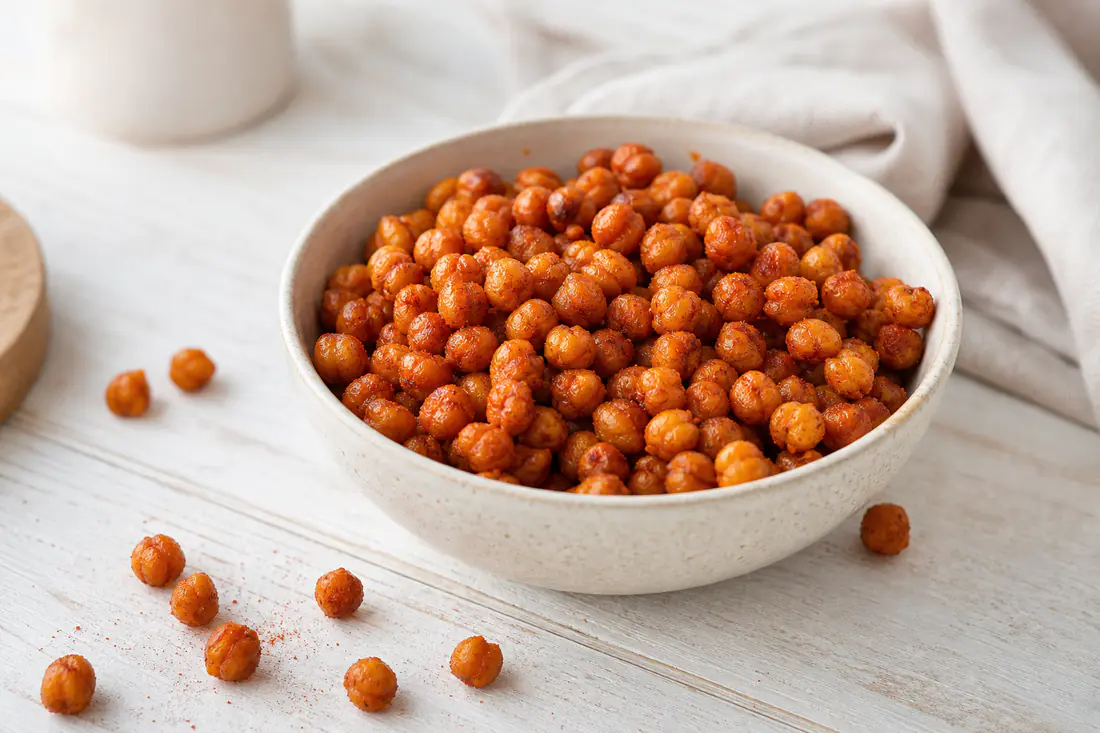Ceci croccanti e dorati con paprika in una ciotola di ceramica, alcuni sparsi sul tavolo di legno