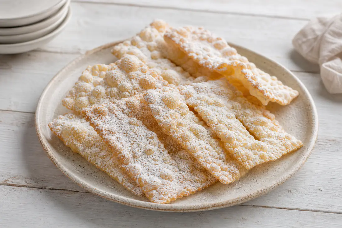 Chiacchiere di Carnevale a nastro, chiare e bollose, cosparse di zucchero a velo, su un piatto da portata