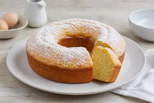 Ciambellone a forma di anello con buco centrale, dorato e spolverato di zucchero a velo, una fetta tagliata che mostra la mollica soffice