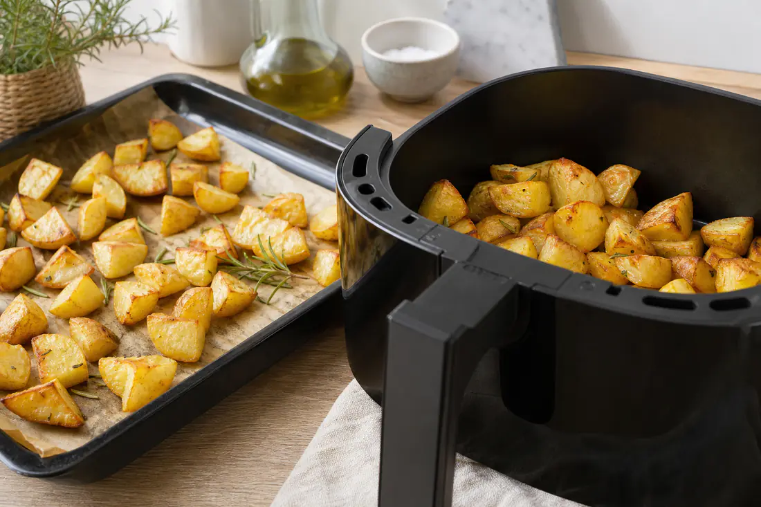 Teglia di patate al forno dorate accanto al cestello di una friggitrice ad aria con patate croccanti