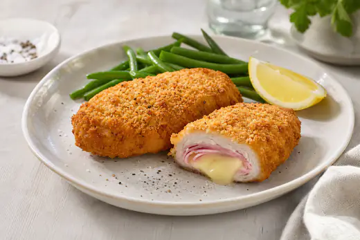 Due cordon bleu di pollo dorati con panatura croccante, uno tagliato a metà con formaggio fuso e prosciutto cotto, serviti con spicchio di limone e fagiolini