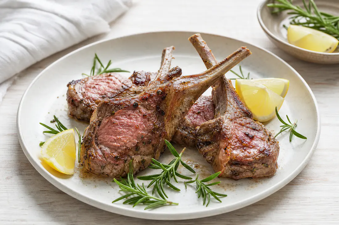 Costolette di agnello con l’osso, dorate e rosate, servite su un piatto con rametti di rosmarino e spicchi di limone