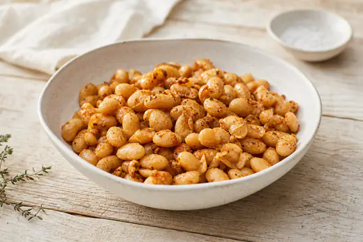 Fagioli cannellini croccanti e dorati, con la pelle leggermente screpolata e spezie, in una ciotola di ceramica