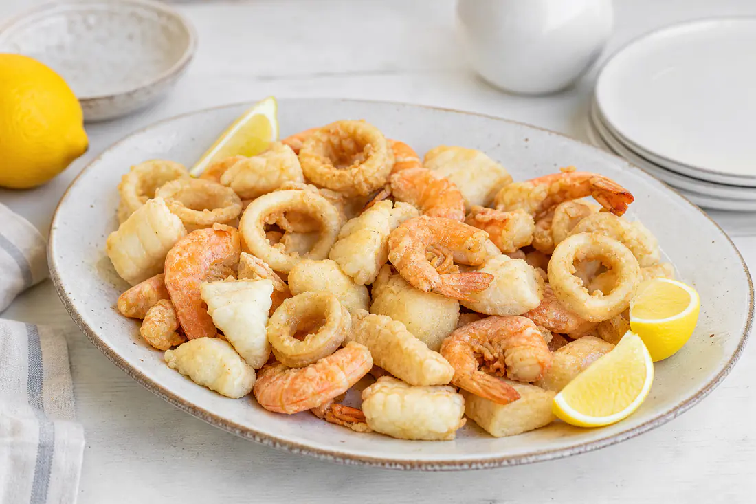 Fritto misto di pesce dorato con anelli di calamari, gamberi e bocconcini di merluzzo infarinati, servito con spicchi di limone su un piatto
