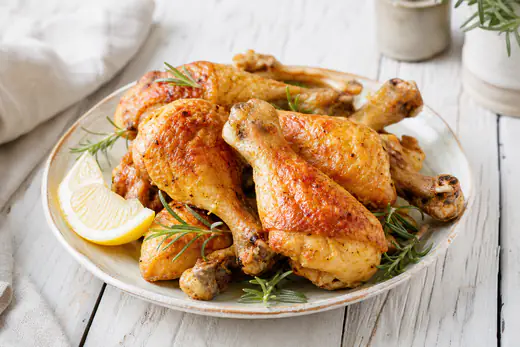 Fusi di pollo dorati e croccanti con l’osso in vista, serviti su un piatto rustico con spicchio di limone e rosmarino fresco
