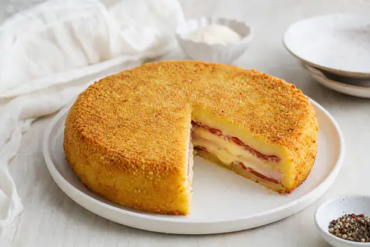 Gateau di patate rotondo sformato su un piatto, con crosta dorata di pangrattato e una fetta tagliata che mostra salame, prosciutto e provola filante