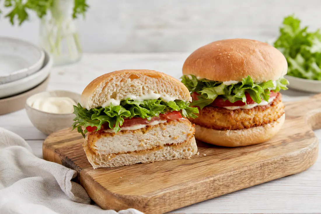 Due hamburger di pollo dorati in un panino morbido con lattuga, pomodoro e salsa, serviti su un tagliere