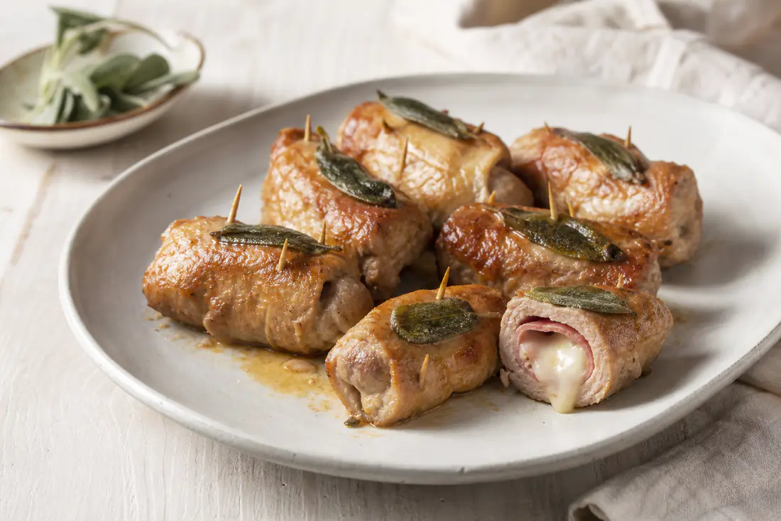 Involtini di carne di vitello arrotolati con prosciutto e formaggio fuso, fermati con stuzzicadenti e foglie di salvia, dorati su un piatto