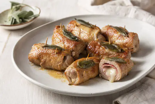Involtini di carne di vitello arrotolati con prosciutto e formaggio fuso, fermati con stuzzicadenti e foglie di salvia, dorati su un piatto