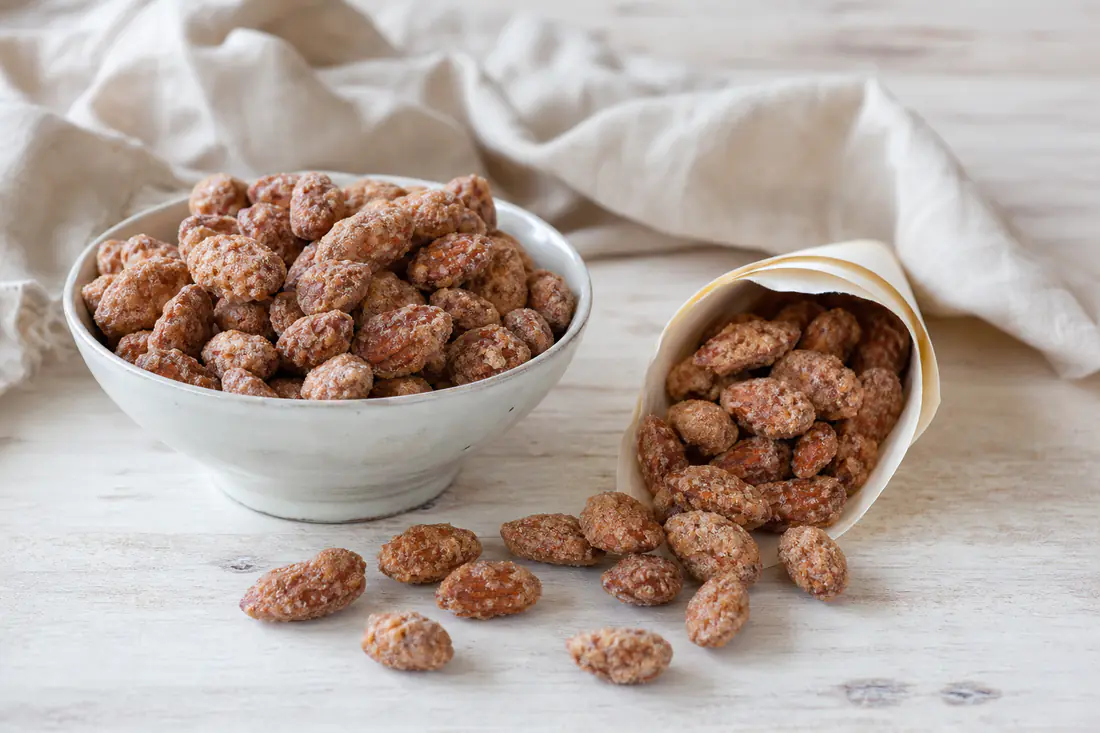 Mandorle pralinate dorate con un rivestimento di zucchero e cannella, versate in un cartoccio di carta e in una ciotolina