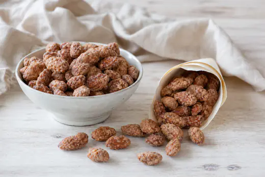 Mandorle pralinate dorate con un rivestimento di zucchero e cannella, versate in un cartoccio di carta e in una ciotolina