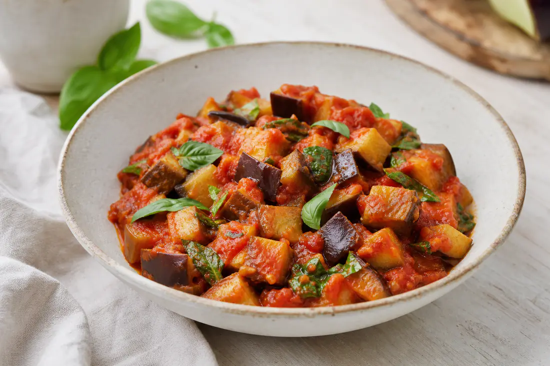 Cubetti di melanzane dorati a funghetto con sugo di pomodoro e foglie di basilico fresco, serviti in un piatto fondo di ceramica