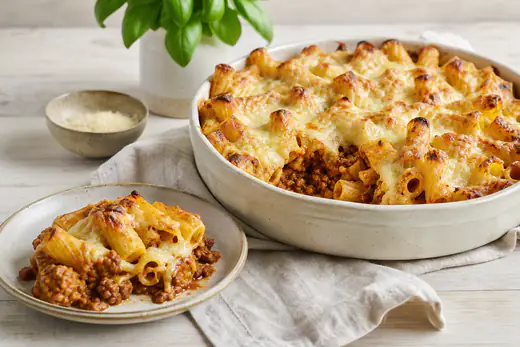 Pasta al forno in una teglia rotonda con rigatoni, ragù e mozzarella gratinata dorata, con punte di pasta croccanti in superficie