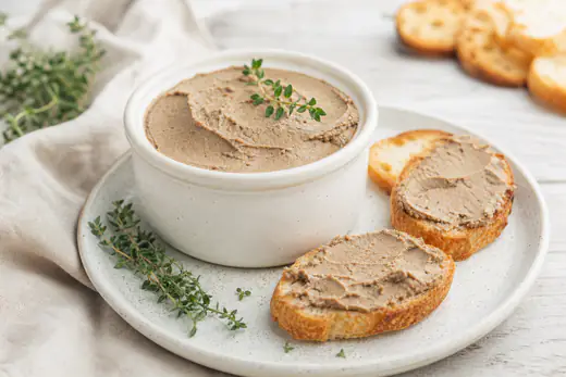 Paté di fegato liscio e cremoso in una ciotolina, spalmato su crostini di pane tostato con rametti di timo