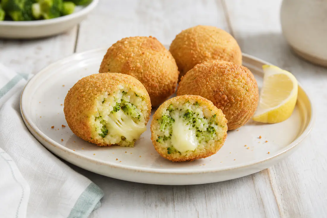 Polpette di broccoli dorate, una tagliata a metà con pezzetti verdi di broccolo e scamorza filante, su un piatto con limone