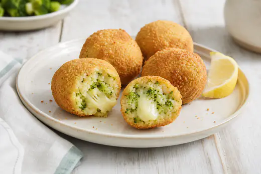 Polpette di broccoli dorate, una tagliata a metà con pezzetti verdi di broccolo e scamorza filante, su un piatto con limone