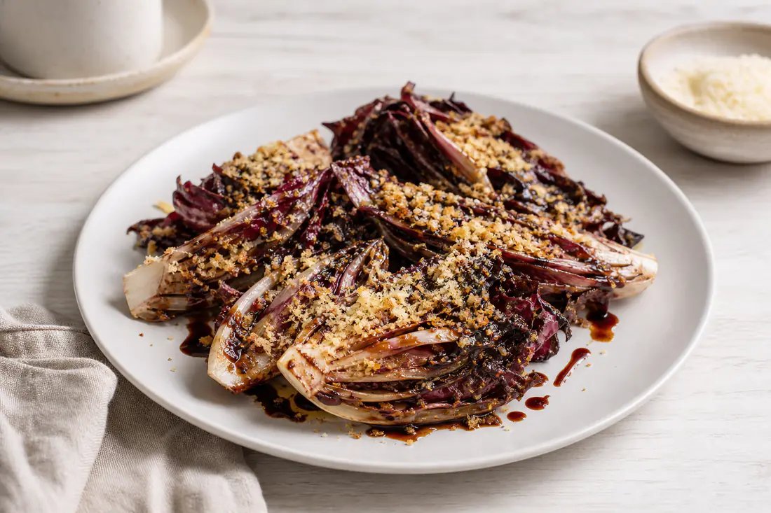 Spicchi di radicchio rosso caramellati con bordi scuri e croccanti e una gratinatura dorata di parmigiano, in un piatto bianco