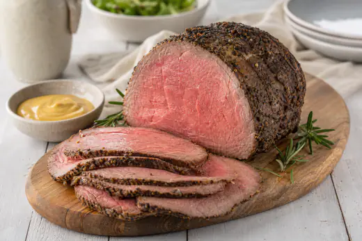 Roast beef affettato sottile con il centro rosato e la crosta scura alle erbe, disposto su un tagliere con rosmarino