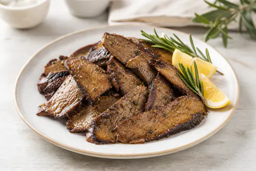 Fette di seitan dorate con bordi scuri e croccanti, lucide di marinata, servite con rosmarino e spicchi di limone