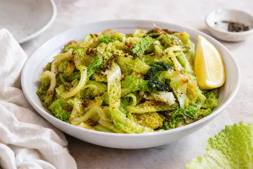 Strisce di verza verde dalle foglie increspate, dorate e croccanti ai bordi, con pepe nero in una ciotola bianca