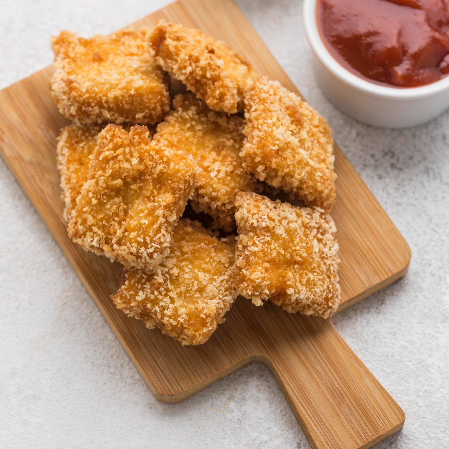 Cubetti di pollo dorati in friggitrice ad aria su un piatto bianco.